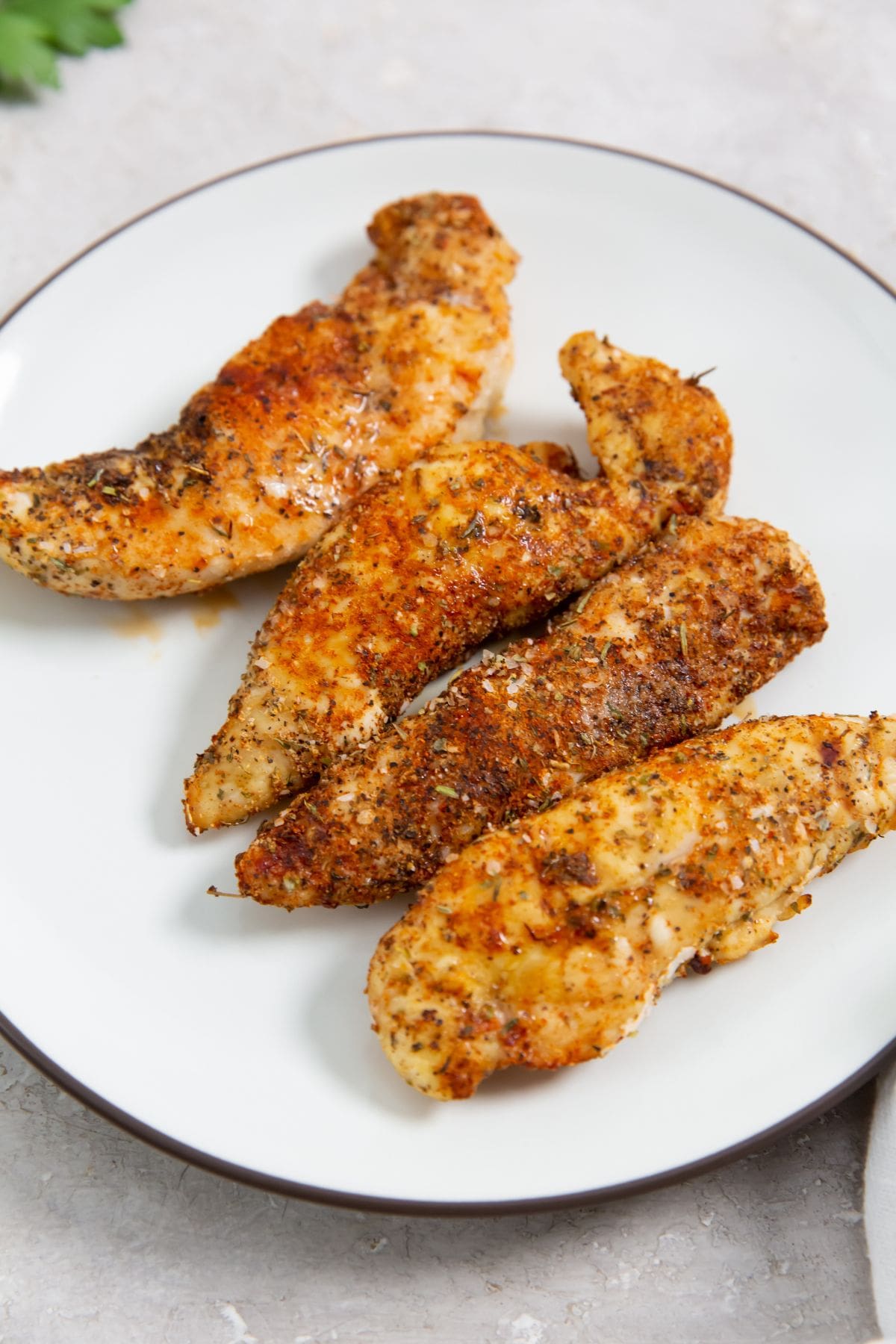 Air Fryer Blackened Chicken Tenders white plate with chicken tenders with parsley. parsley in the back with a towel.