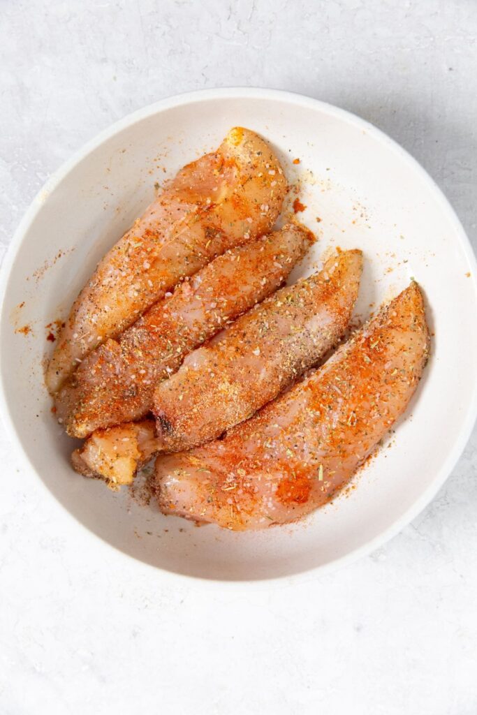Air Fryer Blackened Chicken Tenders white bowl with chicken and seasoning mixed together.