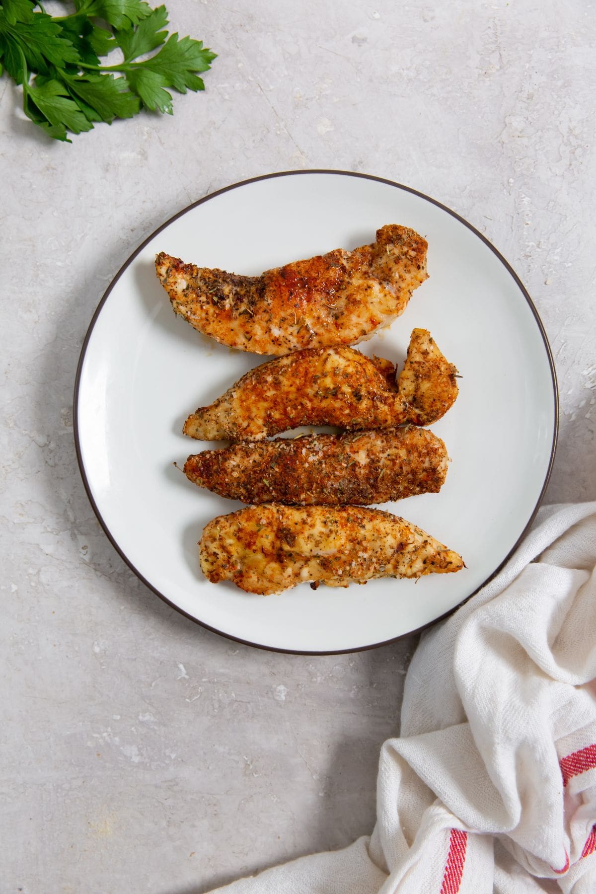 Air Fryer Blackened Chicken Tenders white plate with chicken tenders with parsley. parsley in the back with a towel.