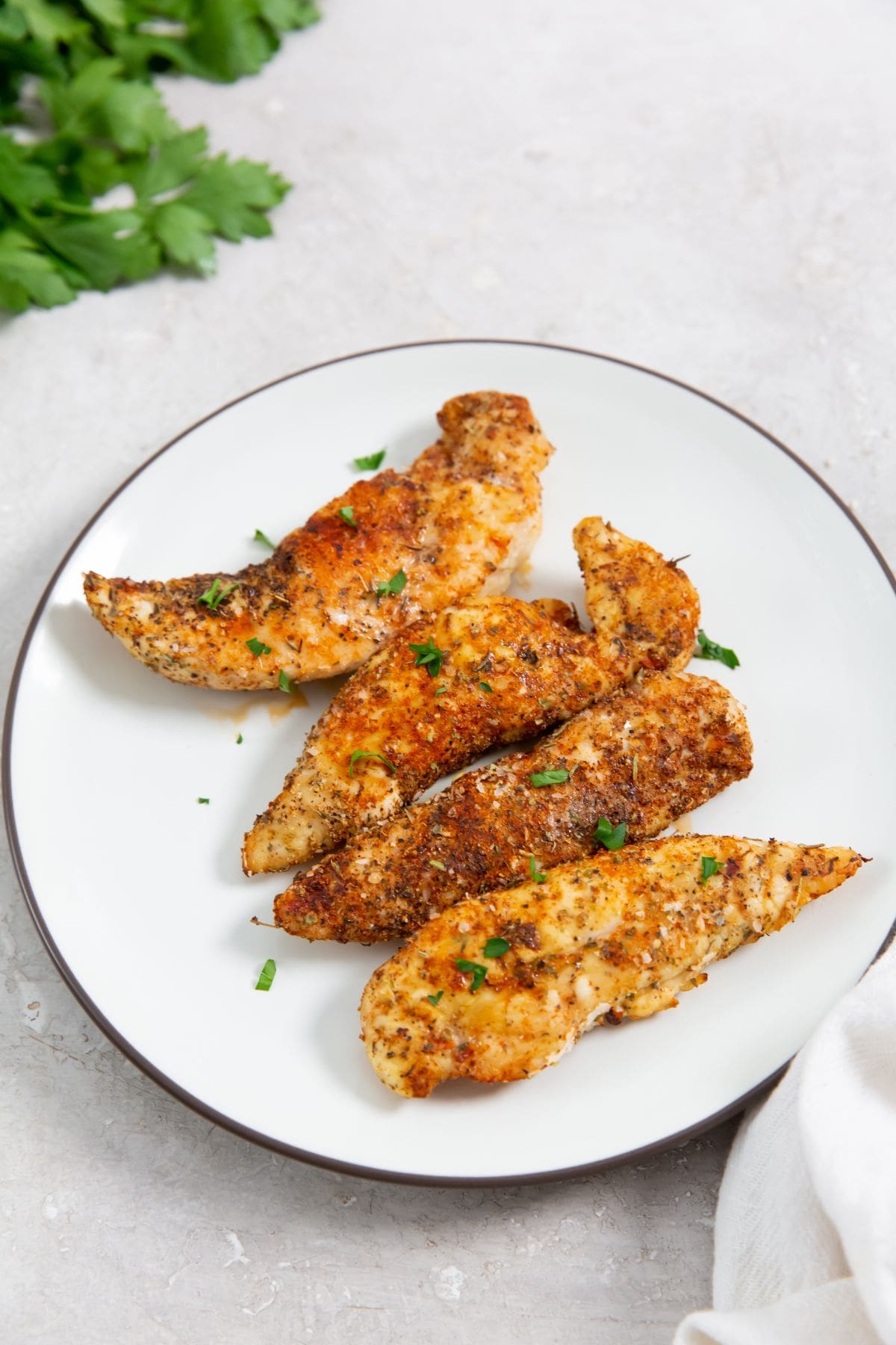 Air Fryer Blackened Chicken Tenders white plate with chicken tenders with parsley. parsley in the back with a towel.