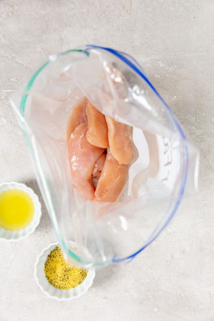 Air Fryer Lemon Pepper Chicken Tenders chicken inside a ziplock bag avocado oil and seasoning next to it.