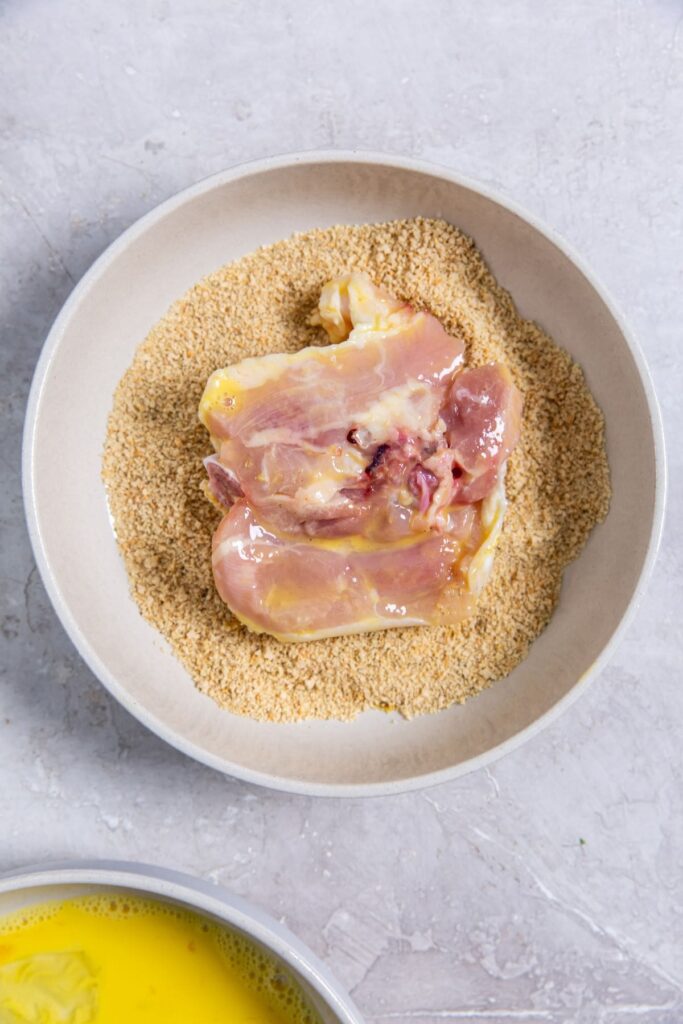 Air Fryer Shake N Bake Chicken Thighs bowl with chicken in the seasoning.