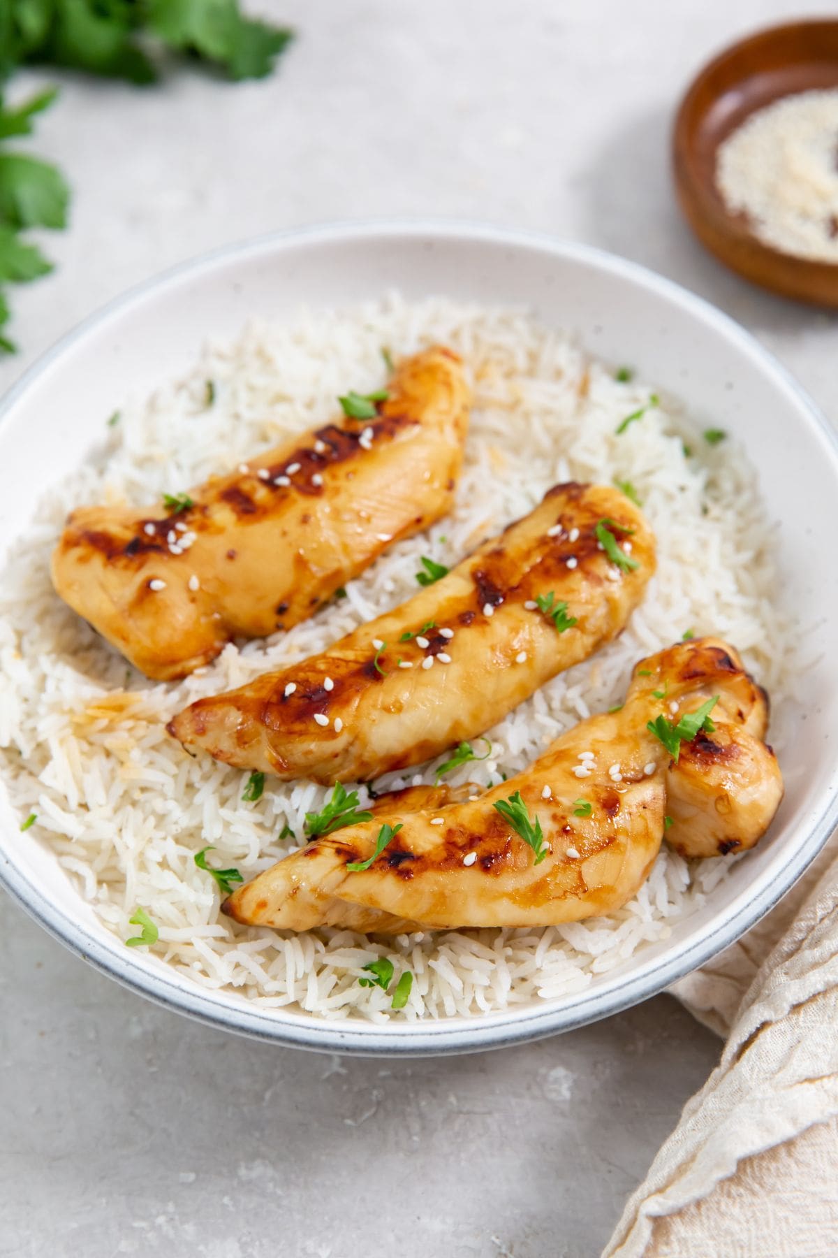 Air Fryer Teriyaki Chicken Tenders white bowl with chicken and rice parsley and towel in the back