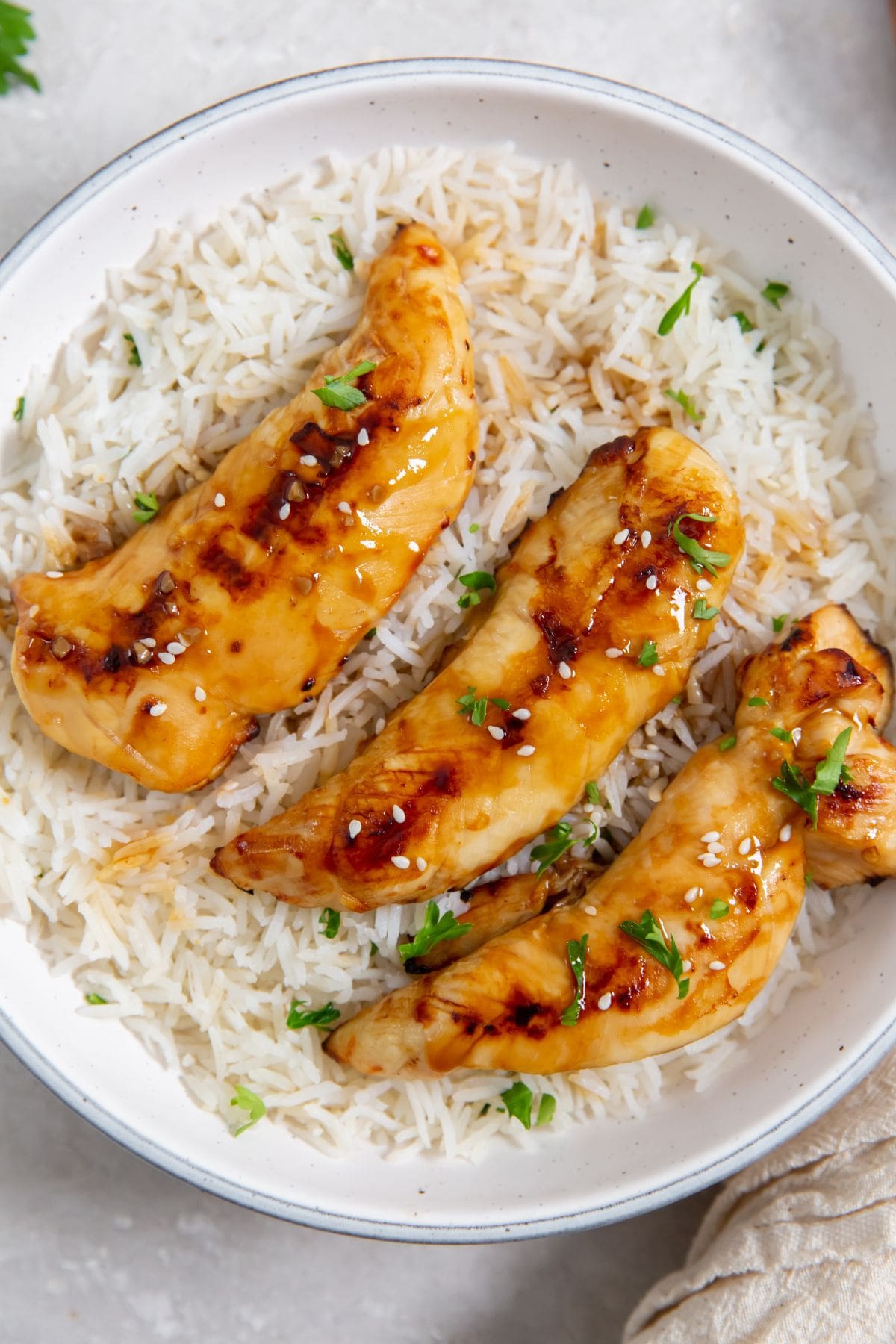 Air Fryer Teriyaki Chicken Tenders white bowl with chicken and rice parsley and towel in the back