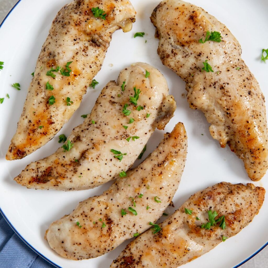 Air Fryer Keto Chicken Tenders chicken on a white plate blue towel underneath . parsley on top and underneath