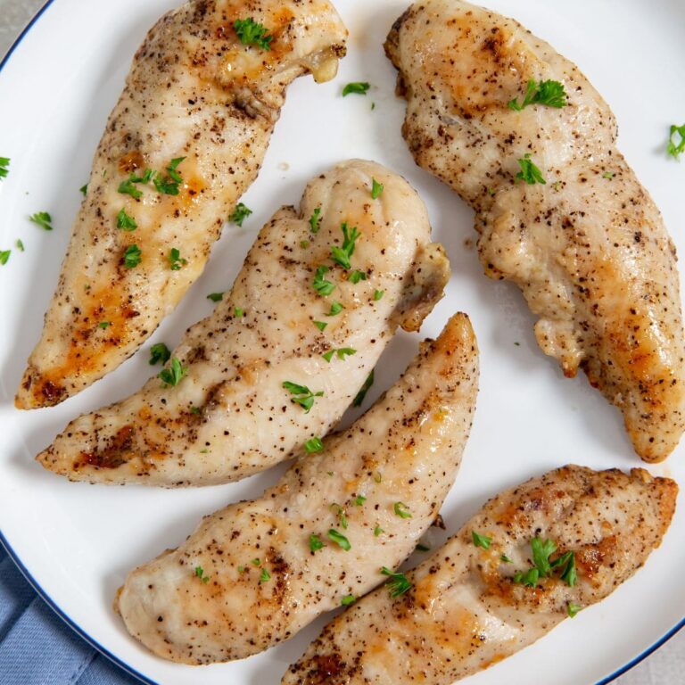 Air Fryer Keto Chicken Tenders chicken on a white plate blue towel underneath . parsley on top and underneath