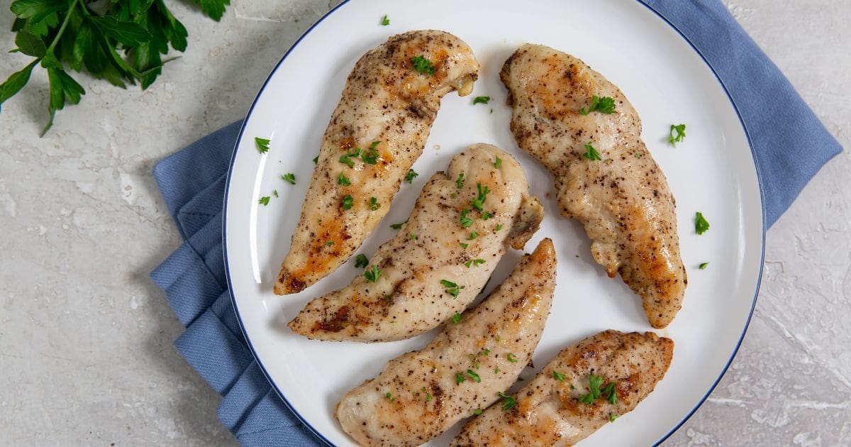 Air Fryer Keto Chicken Tenders chicken on a white plate blue towel underneath . parsley on top and in the back.