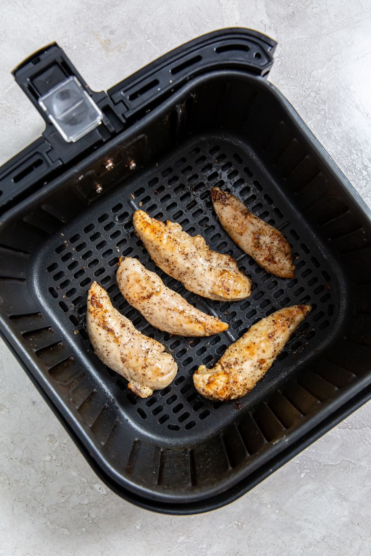 Air Fryer Keto Chicken Tenders black air fryer with the cooked chicken insider.