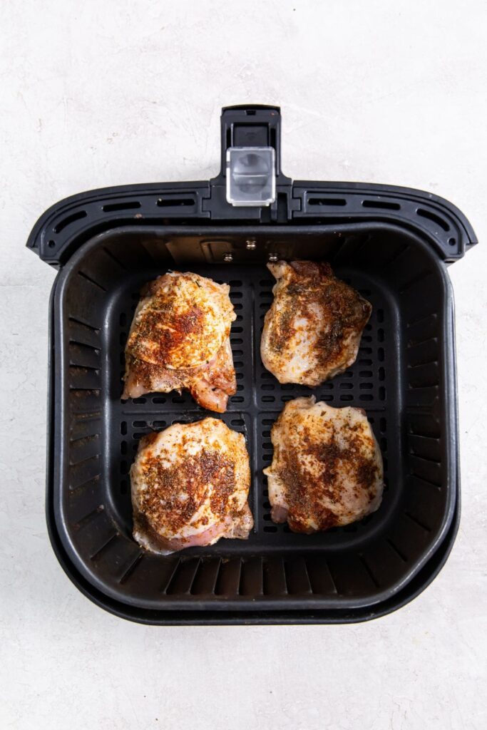 Air Fryer Blackened Chicken Thighs black air fryer basket with raw chicken inside