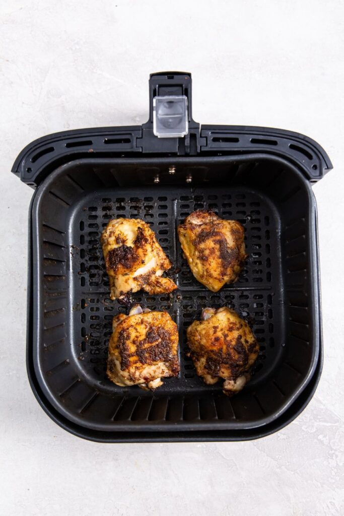 Air Fryer Blackened Chicken Thighs black air fryer basket with cooked chicken inside