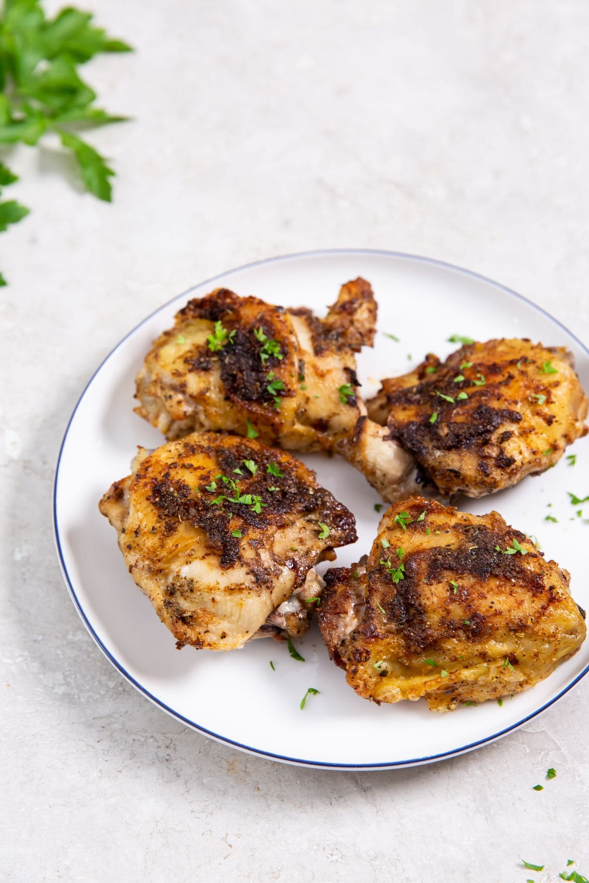 Air Fryer Blackened Chicken Thighs white plate with chicken on it parsley in the back