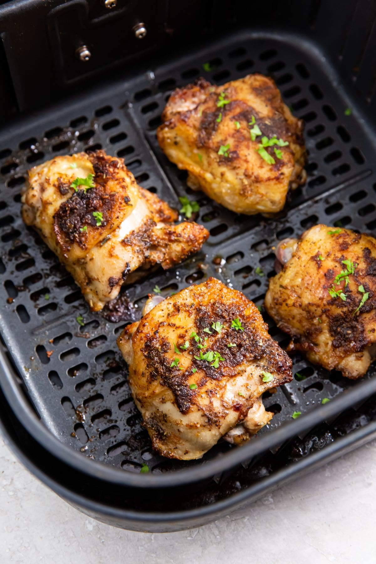 Air Fryer Blackened Chicken Thighs black air fryer basket with cooked chicken inside. parsley sprinkled on top