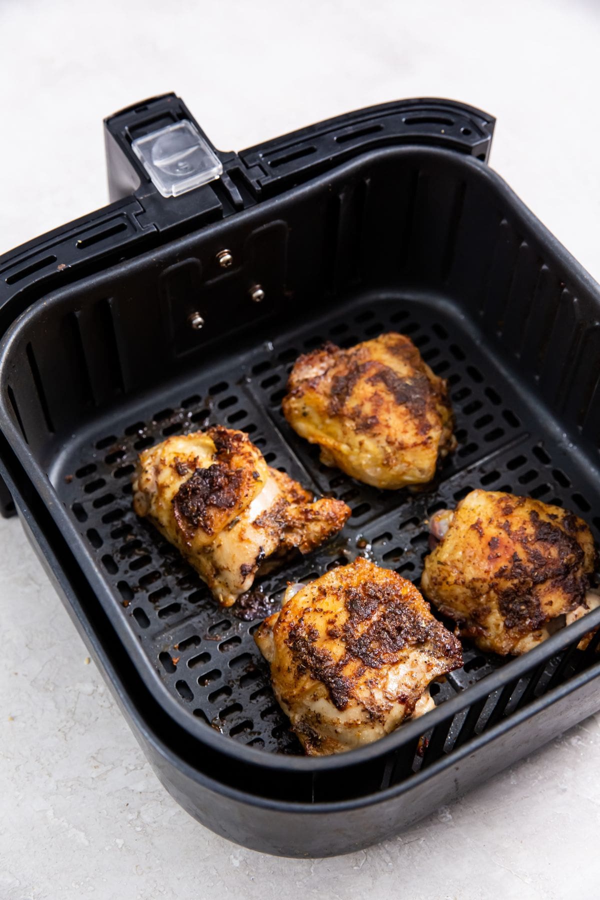 Air Fryer Blackened Chicken Thighs black air fryer basket with cooked chicken inside