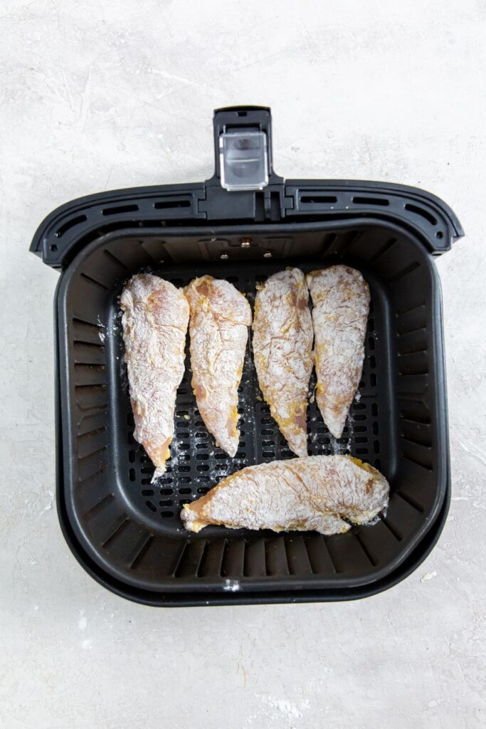 Easy Air Fryer Chicken Tenders With Flour black air fryer basket with raw chicken inside
