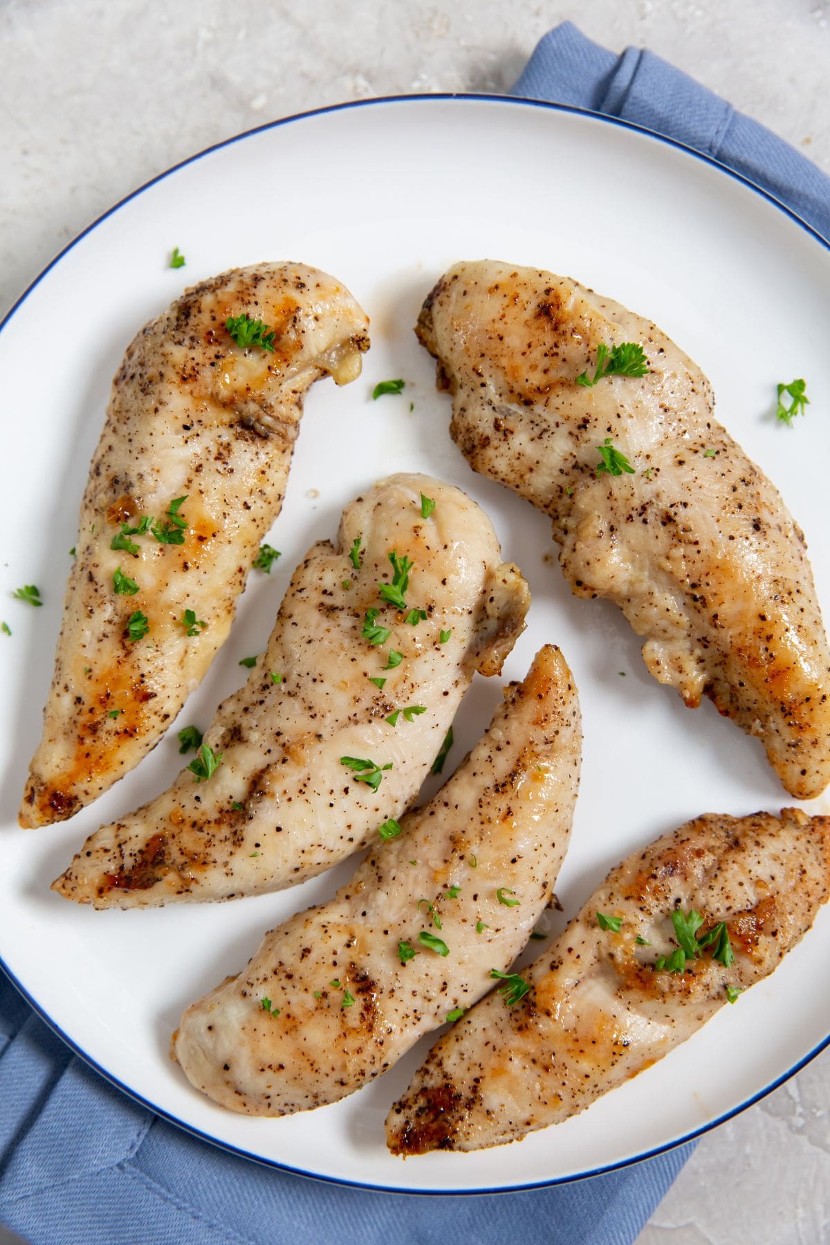 Air Fryer Keto Chicken Tenders chicken on a white plate blue towel underneath parsley on top.
