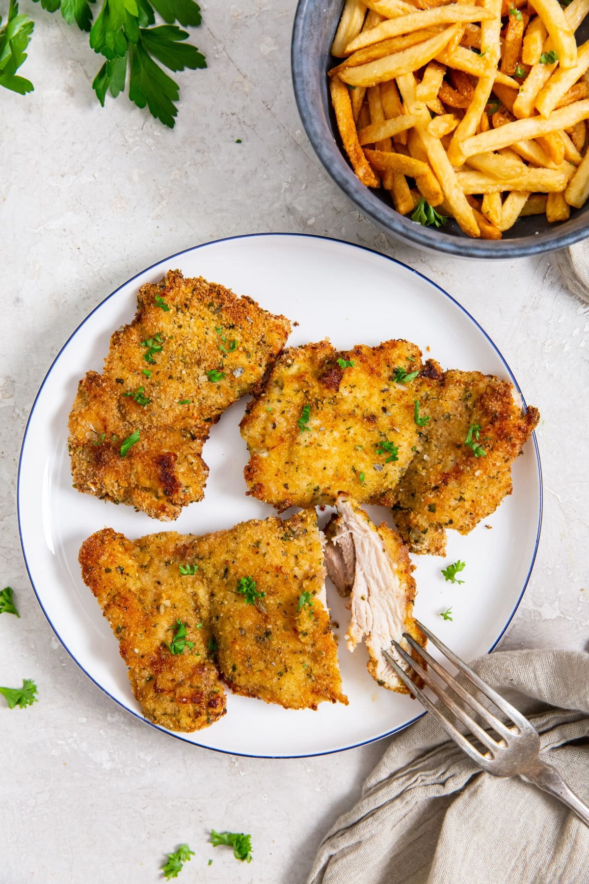 Air Fryer Breaded Chicken Thighs white plate with chicken on it. fries on the side. parsley and towel in the back
