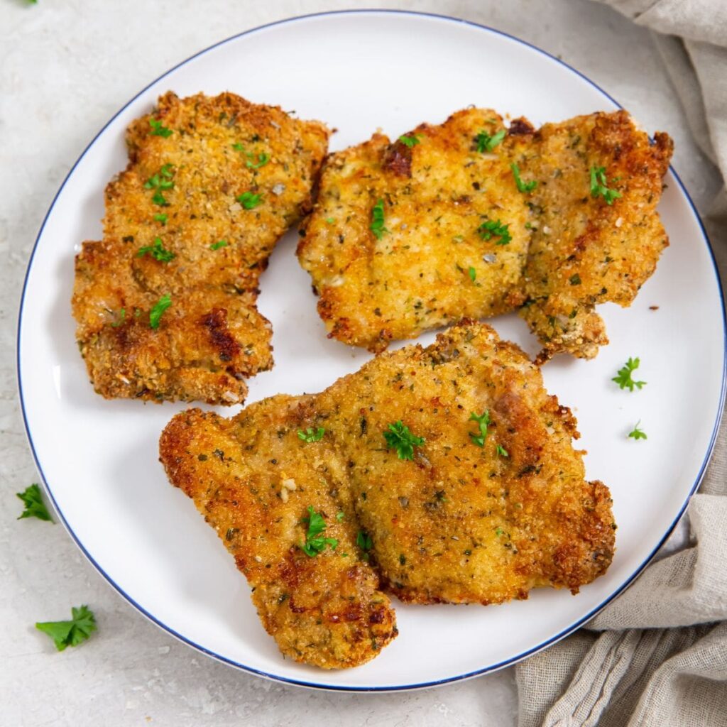 Air Fryer Breaded Chicken Thighs plate with chicken thighs on it. parsley and towel in the back