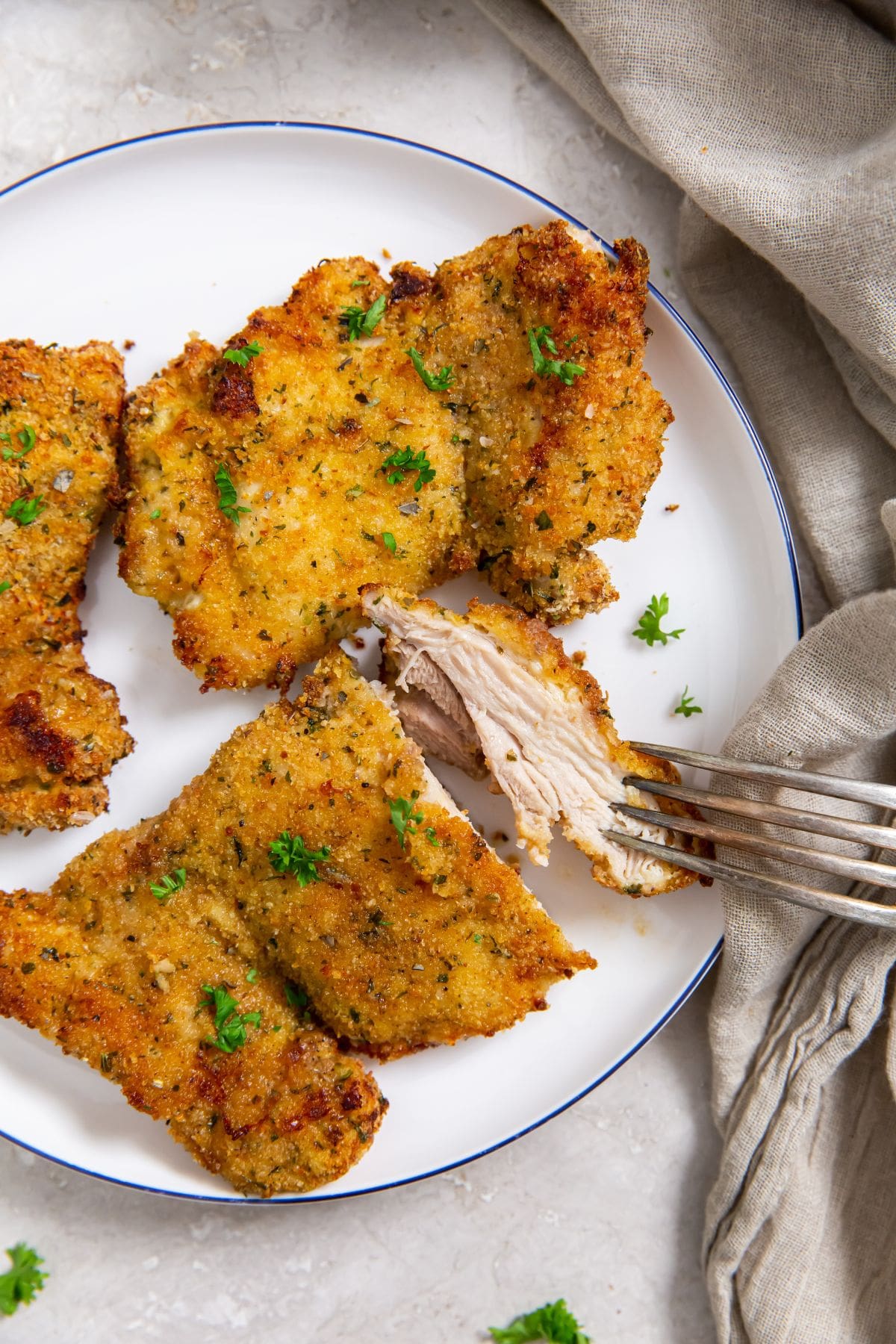 Air Fryer Breaded Chicken Thighs plate with chicken thighs on it. parsley and towel in the back