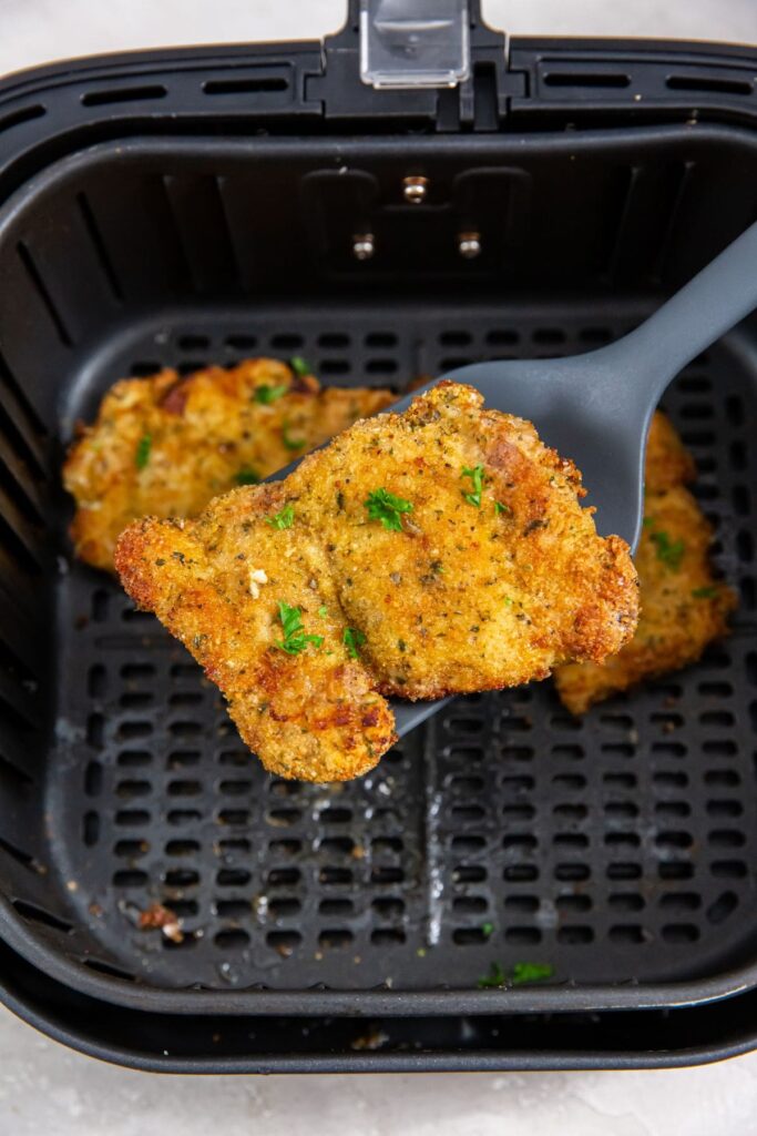 Air Fryer Breaded Chicken Thighs black air fryer with cooked chicken inside. spatula holding chicken
