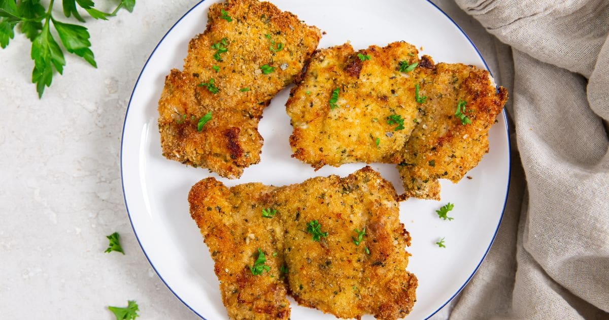 Air Fryer Breaded Chicken Thighs plate with chicken thighs on it. parsley and towel in the back