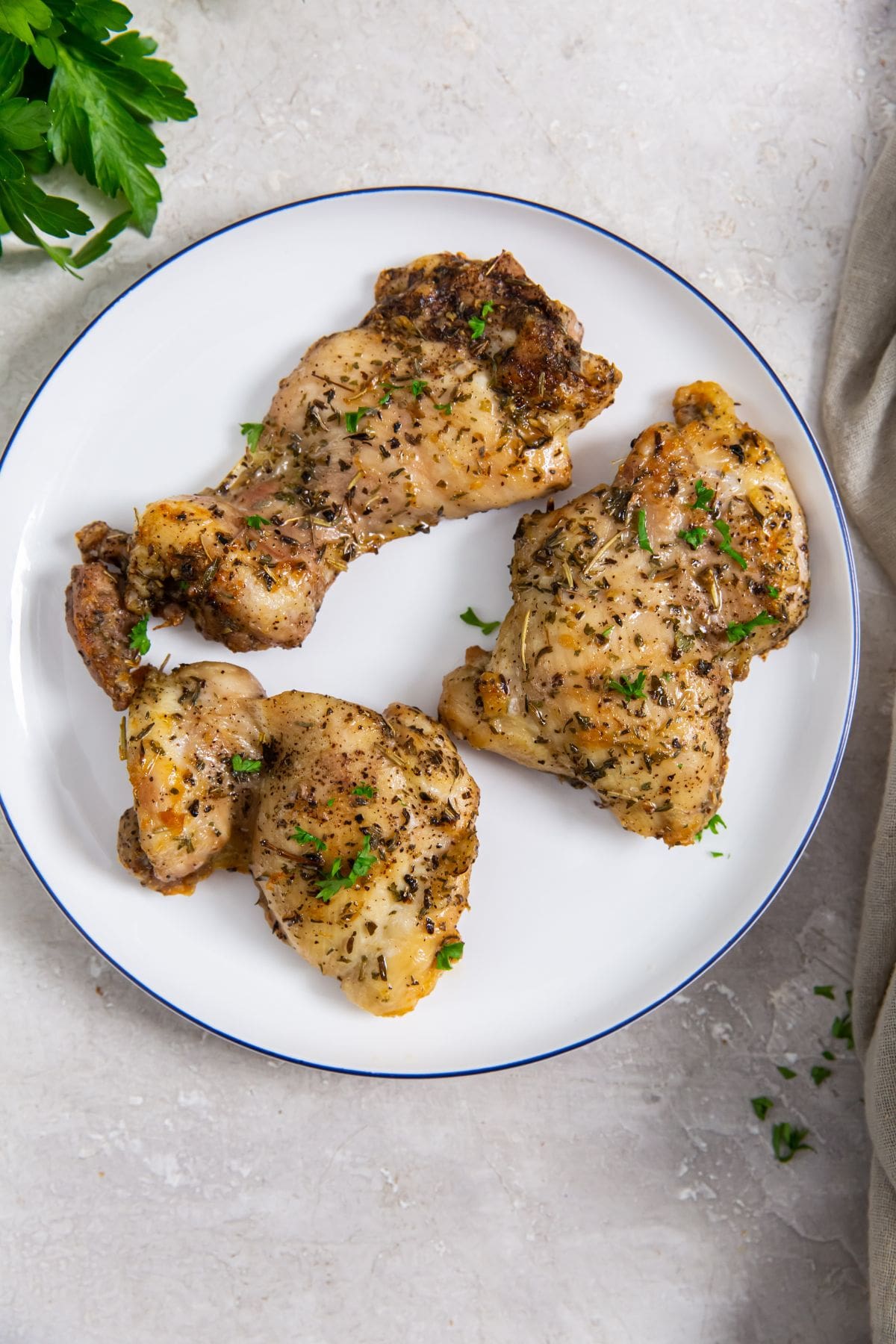 Easy Air Fryer Boneless Skinless Chicken Thighswhite plate with chicken on it. parsley and gray towel in the back.