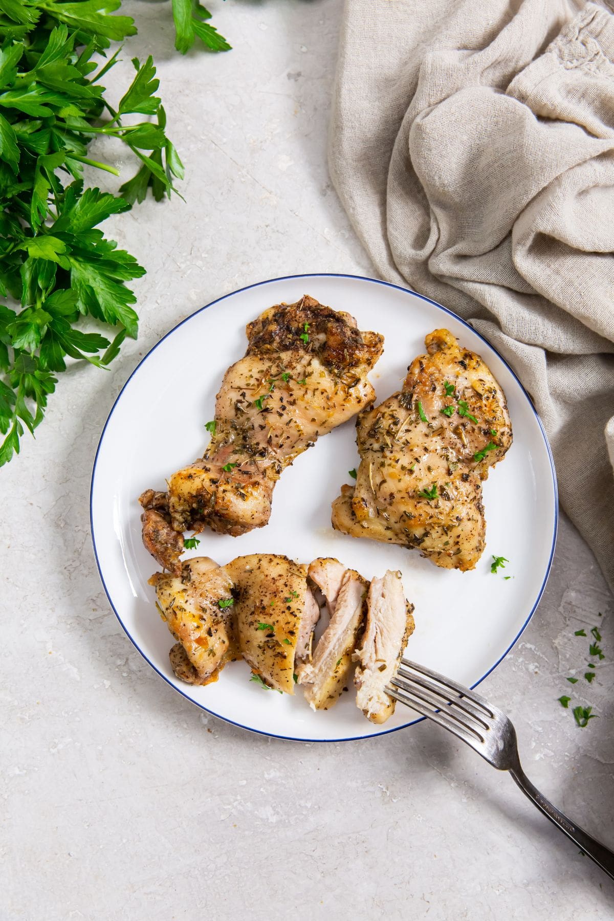 Easy Air Fryer Boneless Skinless Chicken Thighs white plate with chicken on it. parsley and gray towel in the back. fork on the plate