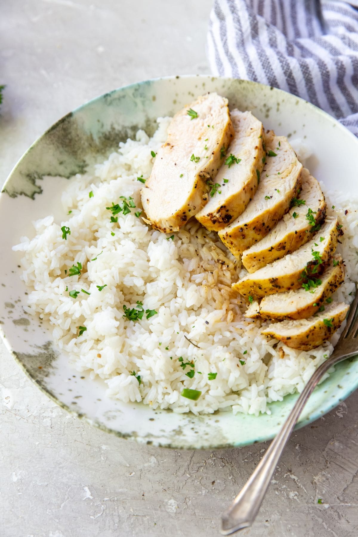 Air Fryer Lemon Pepper Chicken Breasts Grilled chicken breast on a plate with rice and parsley, seasoned with lemon pepper.