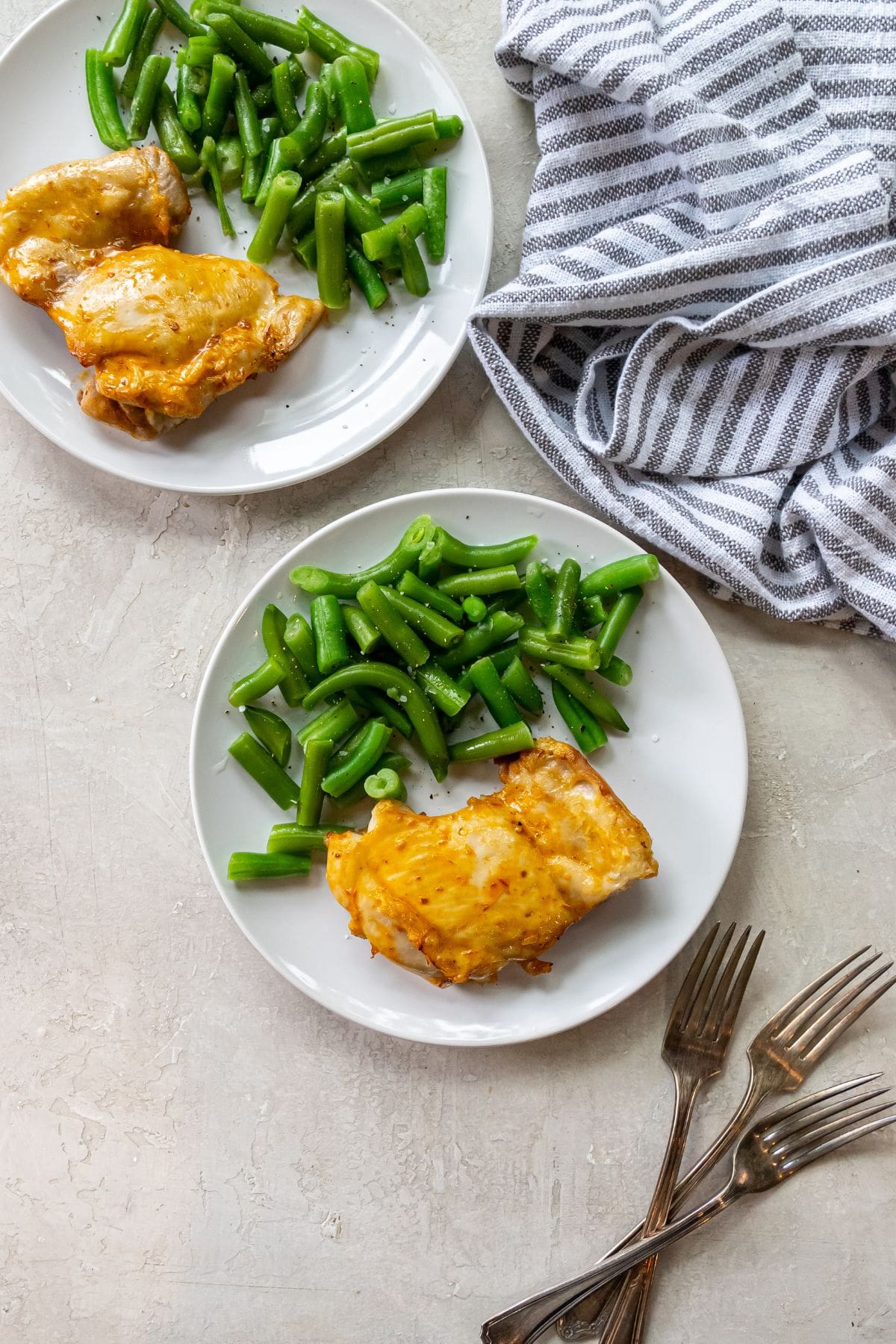 Air Fryer Peri Peri Chicken white plate with chicken and green beans on it. fork next to chicken. striped towel next to plates.