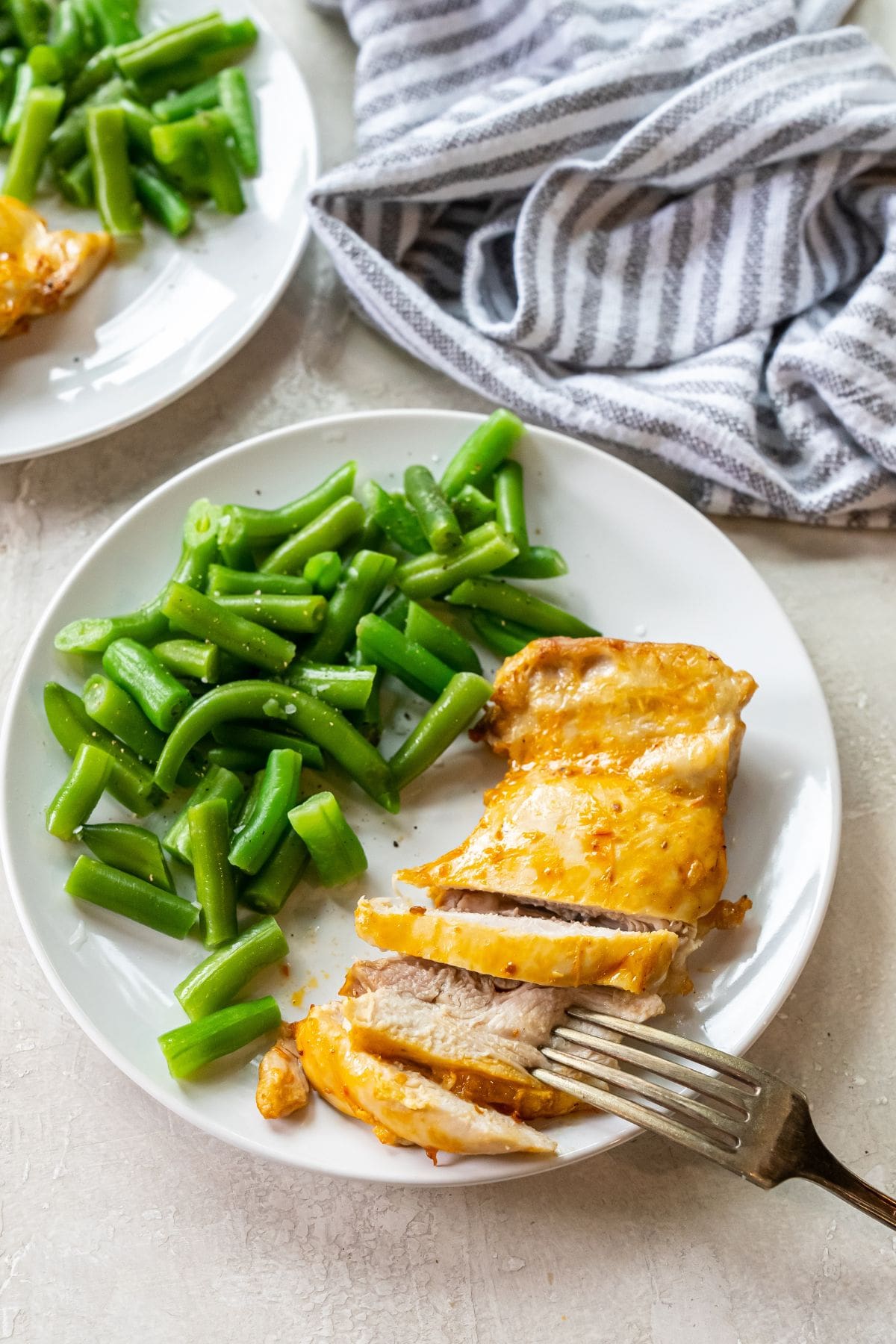 Air Fryer Peri Peri Chicken white plate with chicken and green beans on it. fork next to chicken. striped towel next to plates.