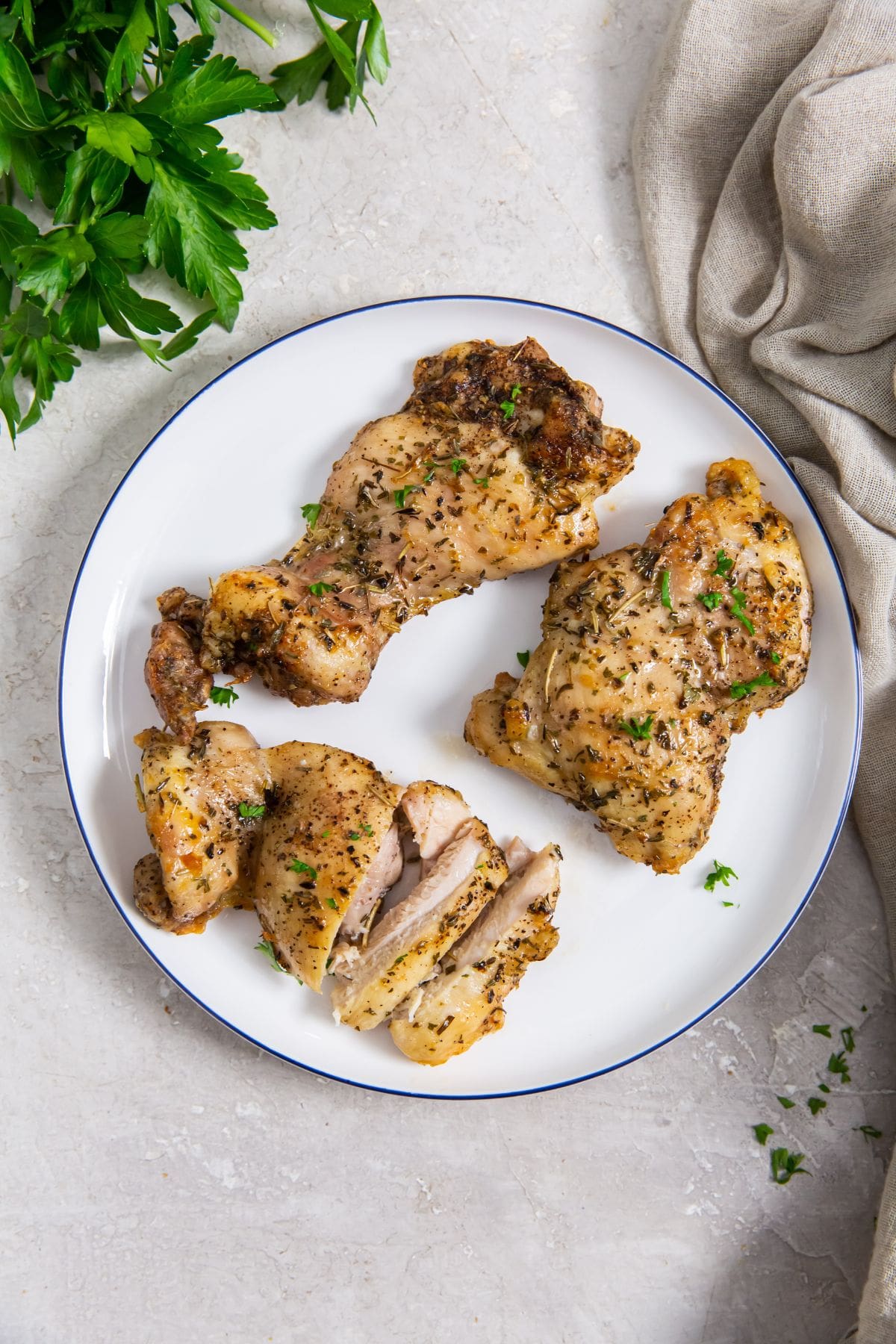 Easy Air Fryer Boneless Skinless Chicken Thighs white plate with chicken on it. parsley and gray towel in the back. fork on the plate