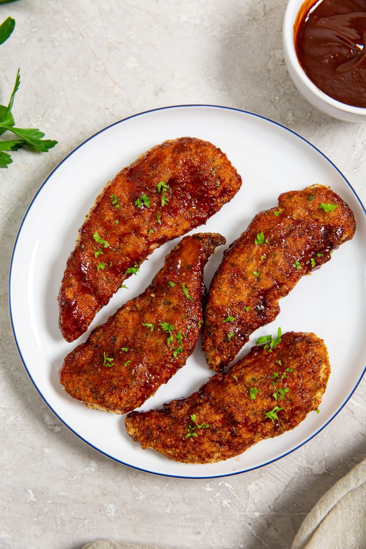 Easy Air Fryer Honey BBQ Chicken Tenders white plate with chicken on it parsley and bbq sauce in the back 