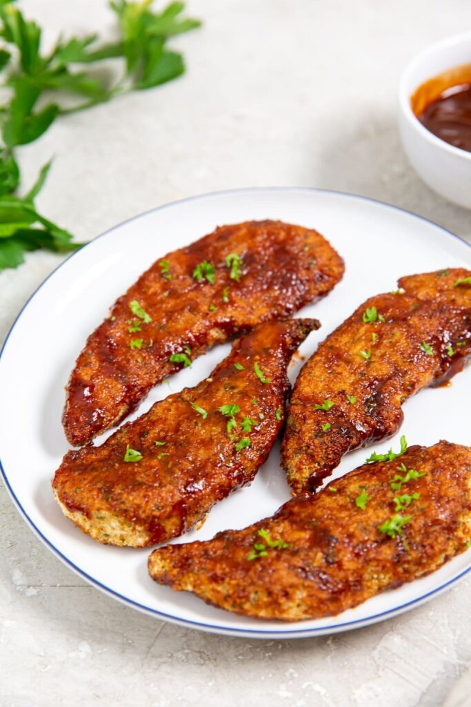 Easy Air Fryer Honey BBQ Chicken Tenders white plate with chicken on it parsley and bbq sauce in the back