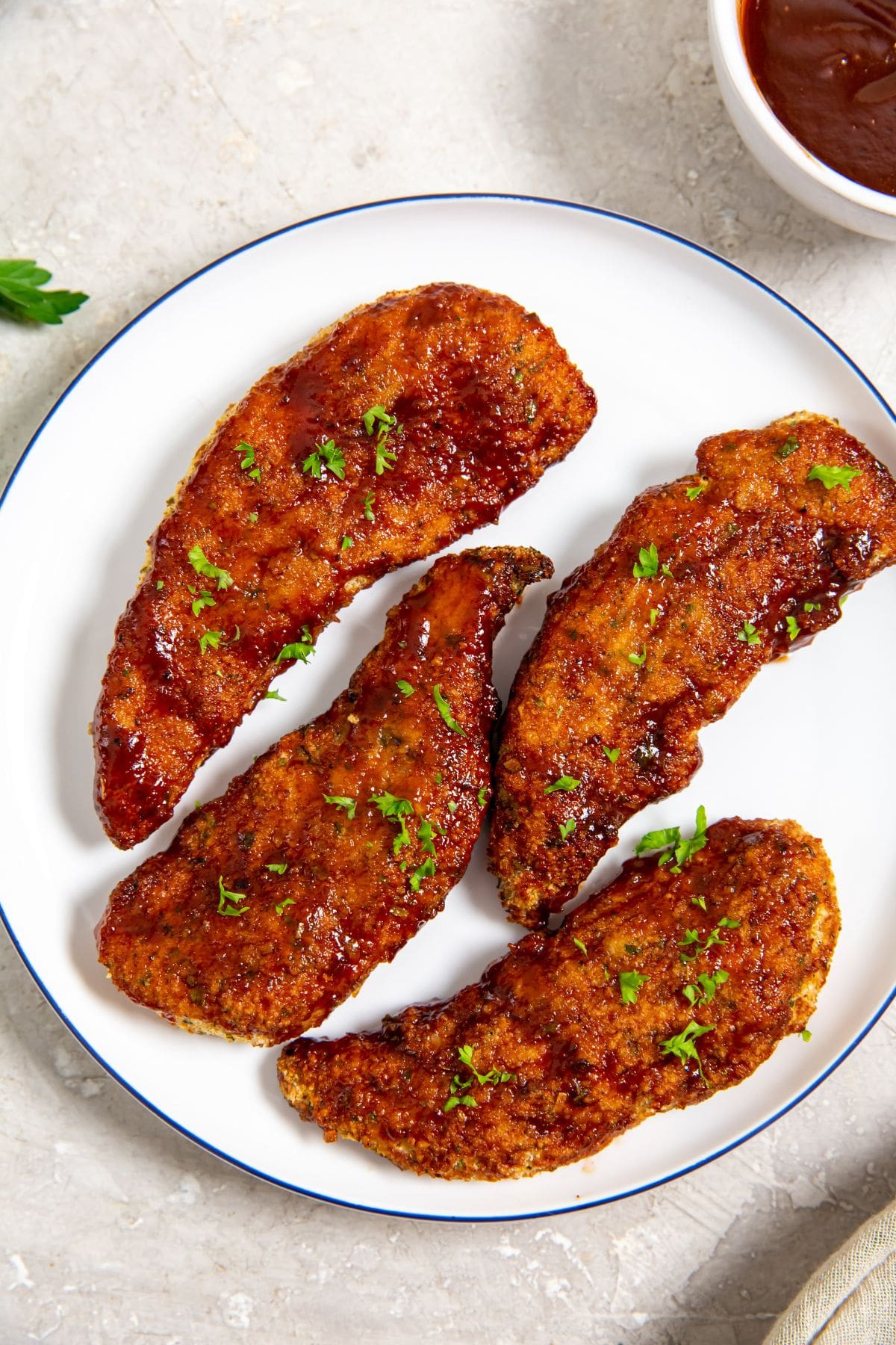 Easy Air Fryer Honey BBQ Chicken Tenders white plate with chicken on it parsley and bbq sauce in the back
