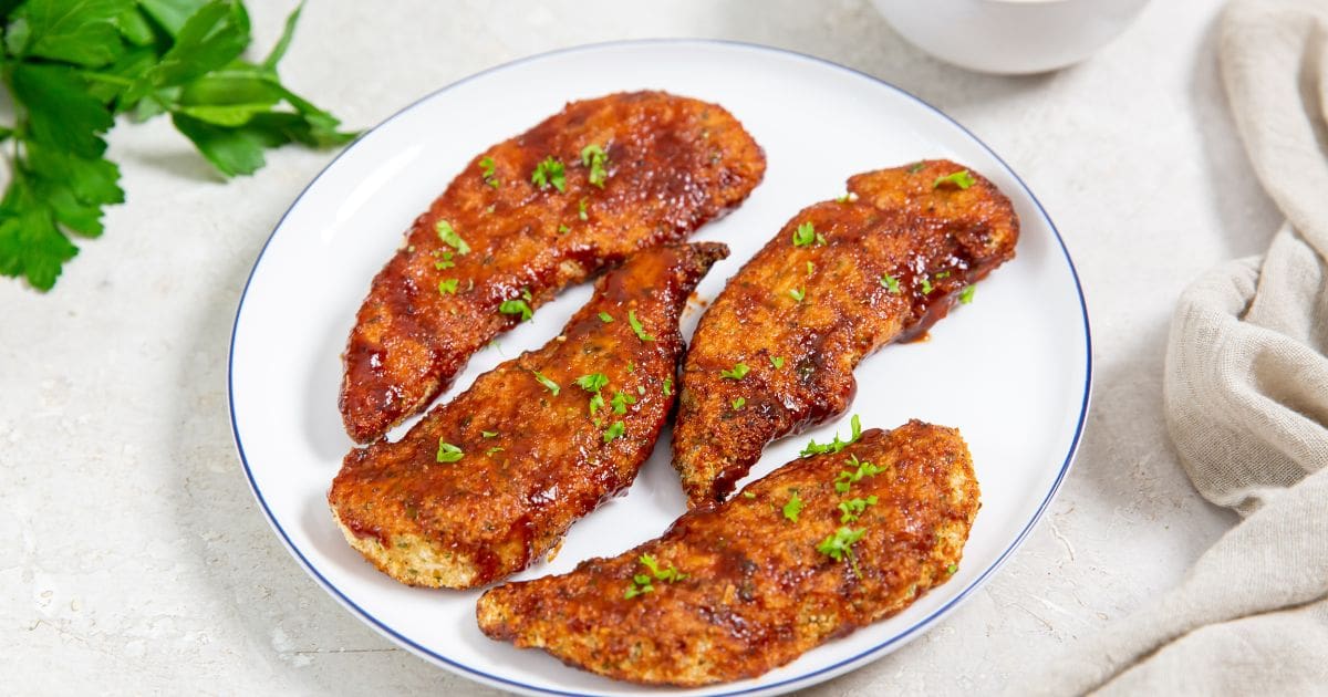 Easy Air Fryer Honey BBQ Chicken Tenders white plate with chicken on it parsley and bbq sauce in the back