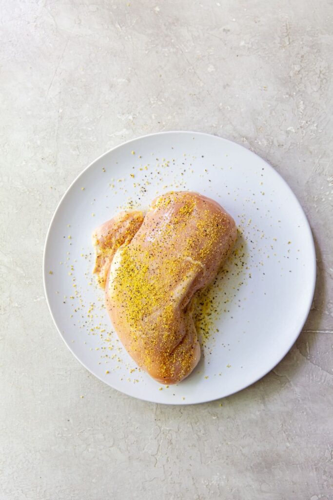 Air Fryer Lemon Pepper Chicken Breasts A lemon pepper chicken breast cooked in an air fryer, presented on a white plate with yellow sprinkles.