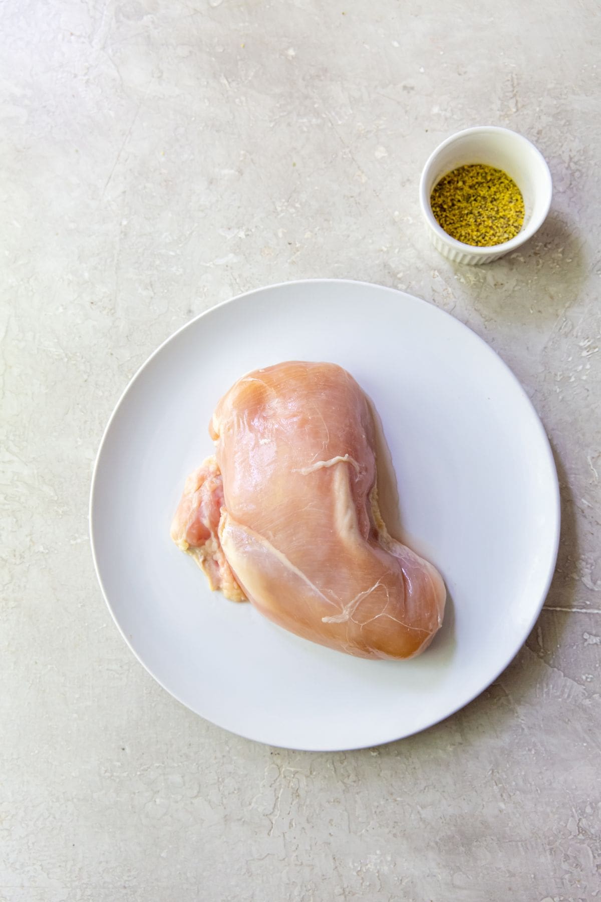 Air Fryer Lemon Pepper Chicken Breasts An air-fried chicken breast on a white plate, seasoned with lemon pepper.