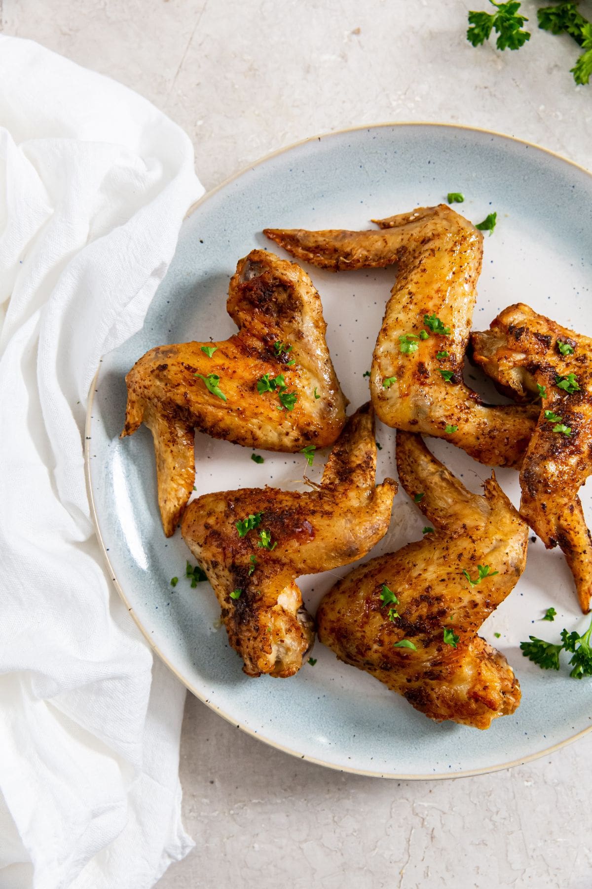 Air Fryer Whole Chicken Wings blue plate with chicken and parsley on it. white towel next to it.