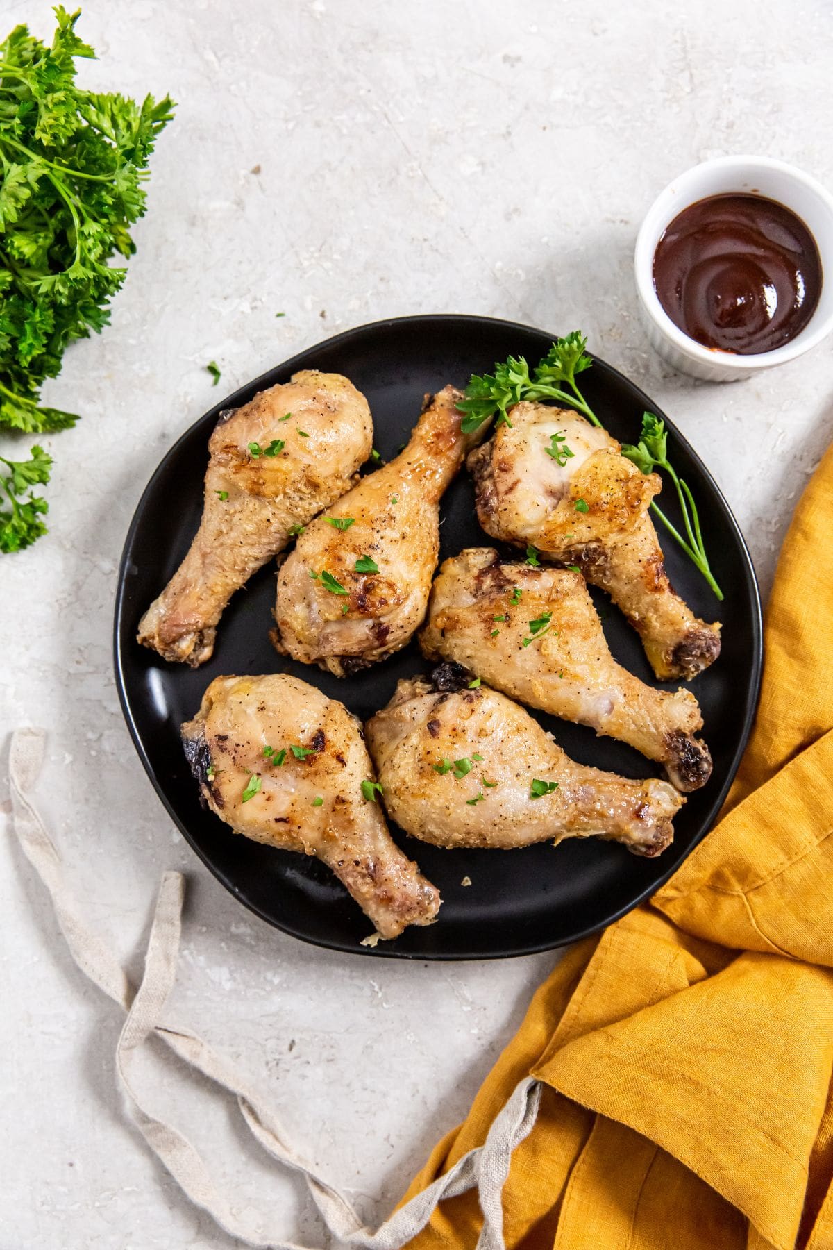 Air Fryer Crispy Chicken Legs black plate with chicken on it. orange plate in the back.