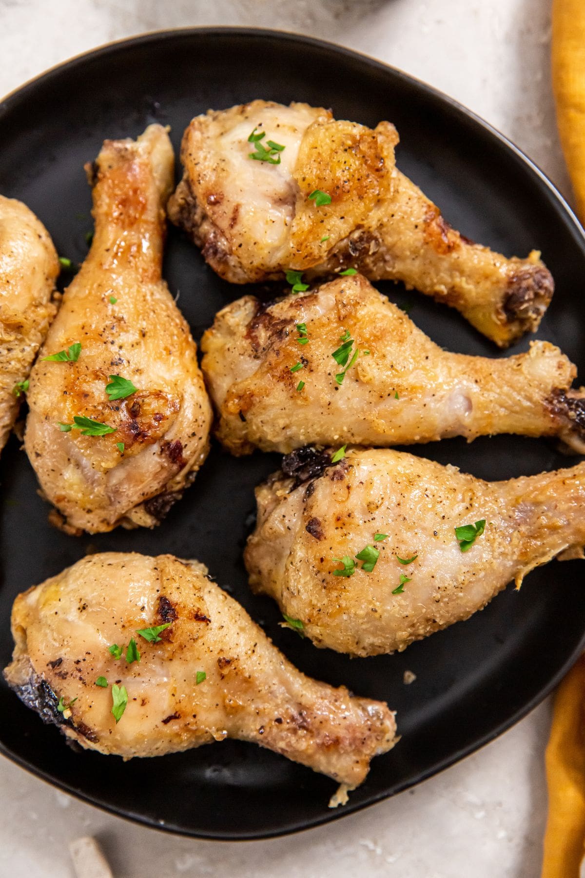 Air Fryer Crispy Chicken Legs black plate with chicken legs on it. orange plate in the back.