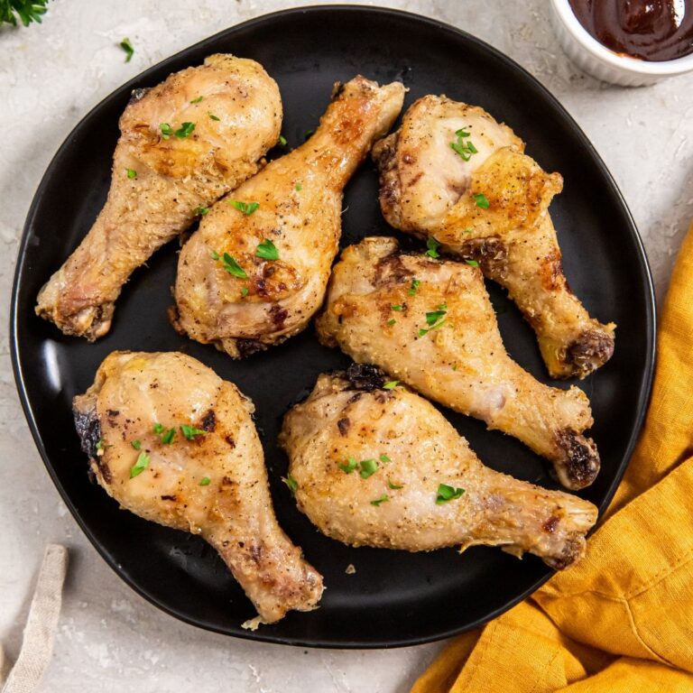 Air Fryer Crispy Chicken Legs black plate of cooked chicken legs next to a burnt orange tea towel and a small ramekin of BBQ sauce for dipping