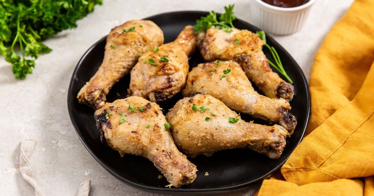 Air Fryer Crispy Chicken Legs black plate with chicken on it. orange plate in the back.