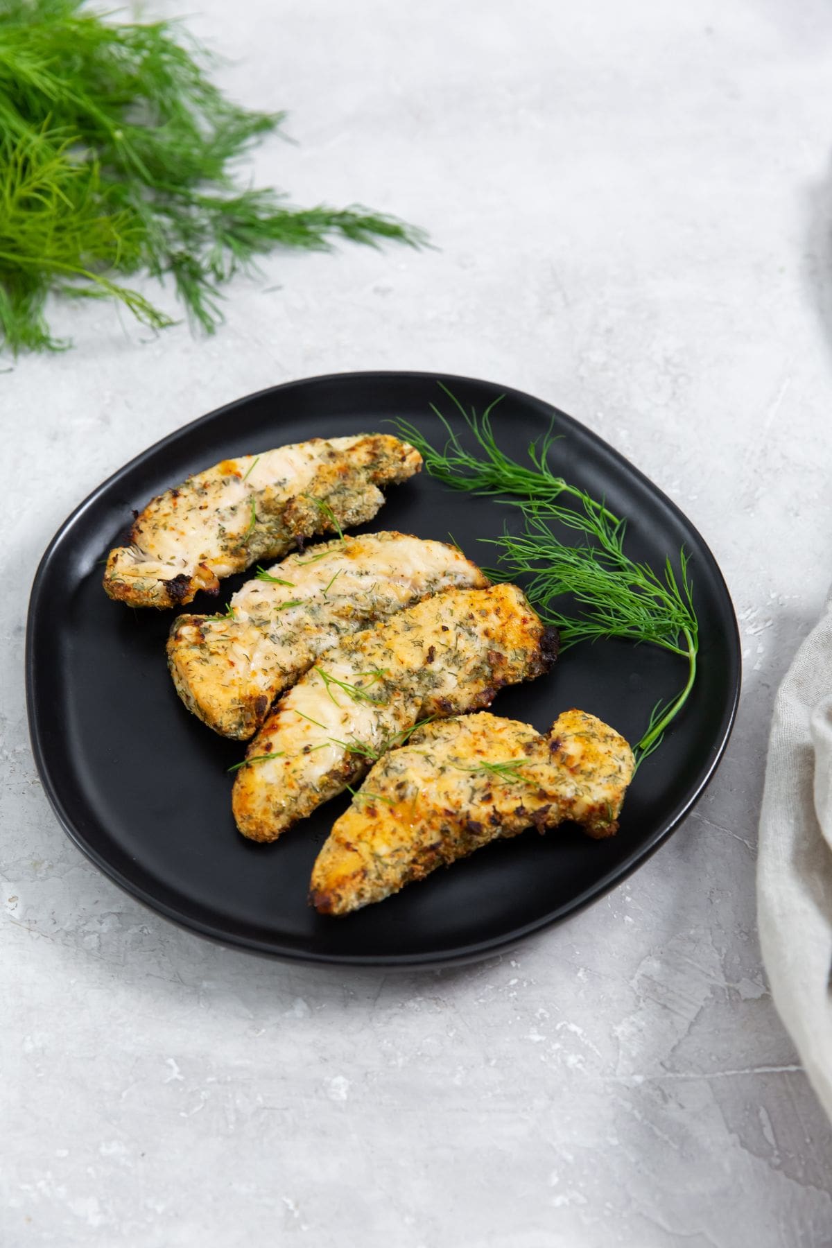 Air Fryer Ranch Chicken Tenders black plate with chicken and dill on it. dill and towel in the back