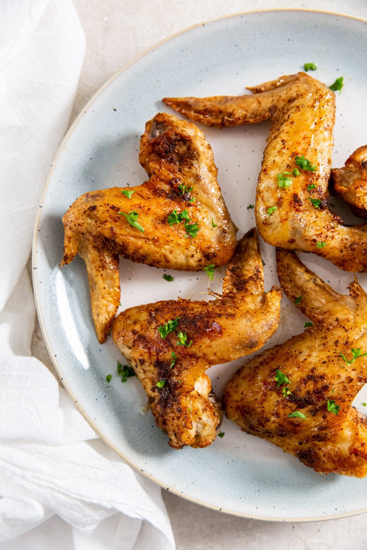 Air Fryer Whole Chicken Wings blue plate with chicken and parsley on it. White towel next to it.