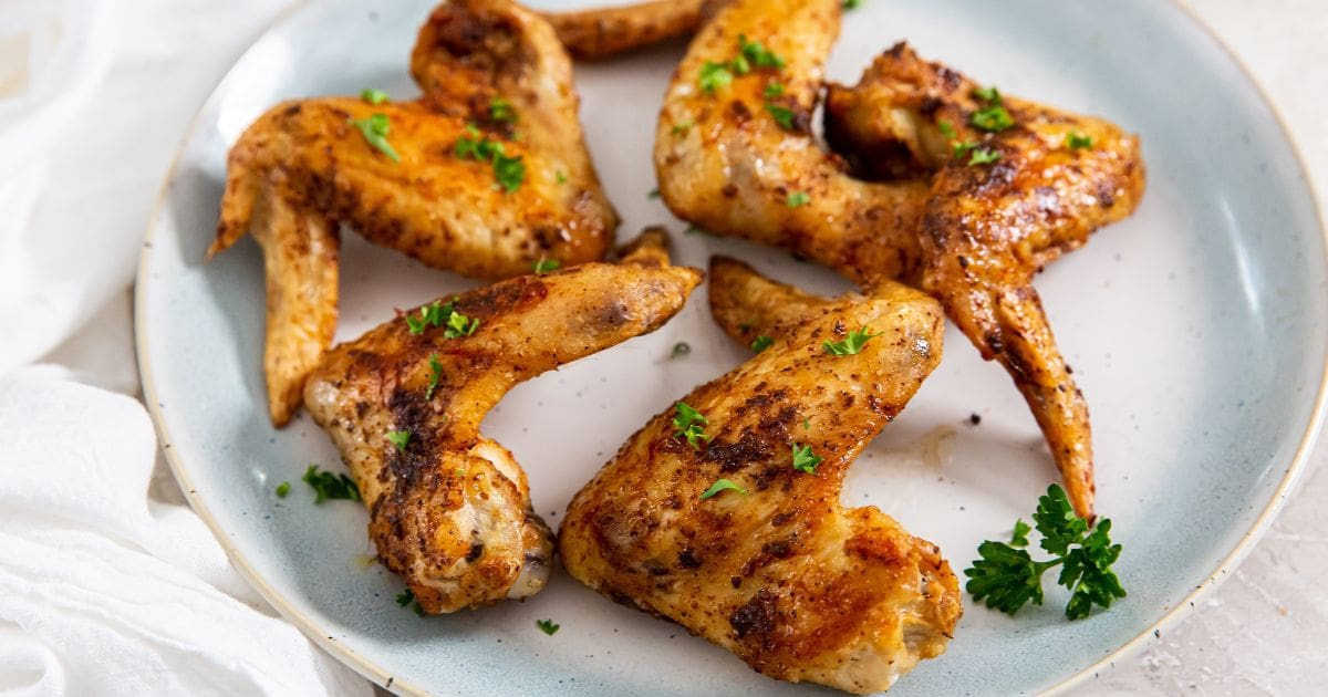 Air Fryer Whole Chicken Wings blue plate with chicken and parsley on it. White towel next to it