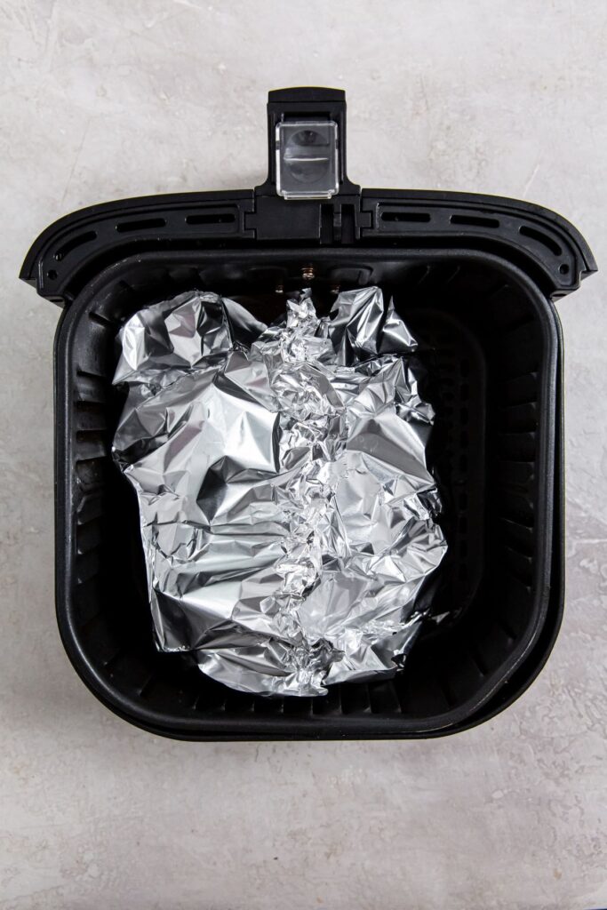 Easy Air Fryer Chicken Legs with Dry Rub black air fryer with aluminum foil and chicken wrapped inside.