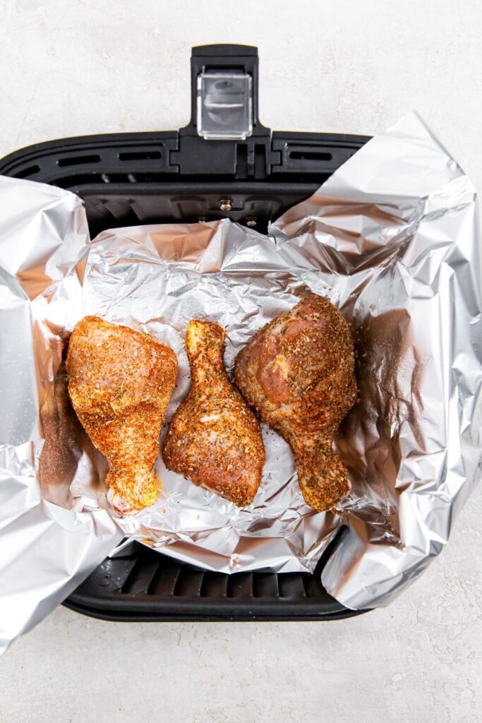 Easy Air Fryer Chicken Legs with Dry Rub black air fryer with aluminum foil and raw chicken inside