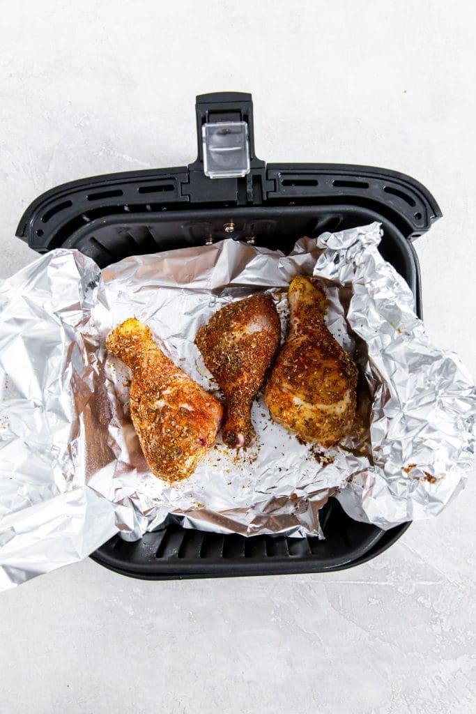 Easy Air Fryer Chicken Legs with Dry Rub black air fryer with aluminum foil and raw chicken inside