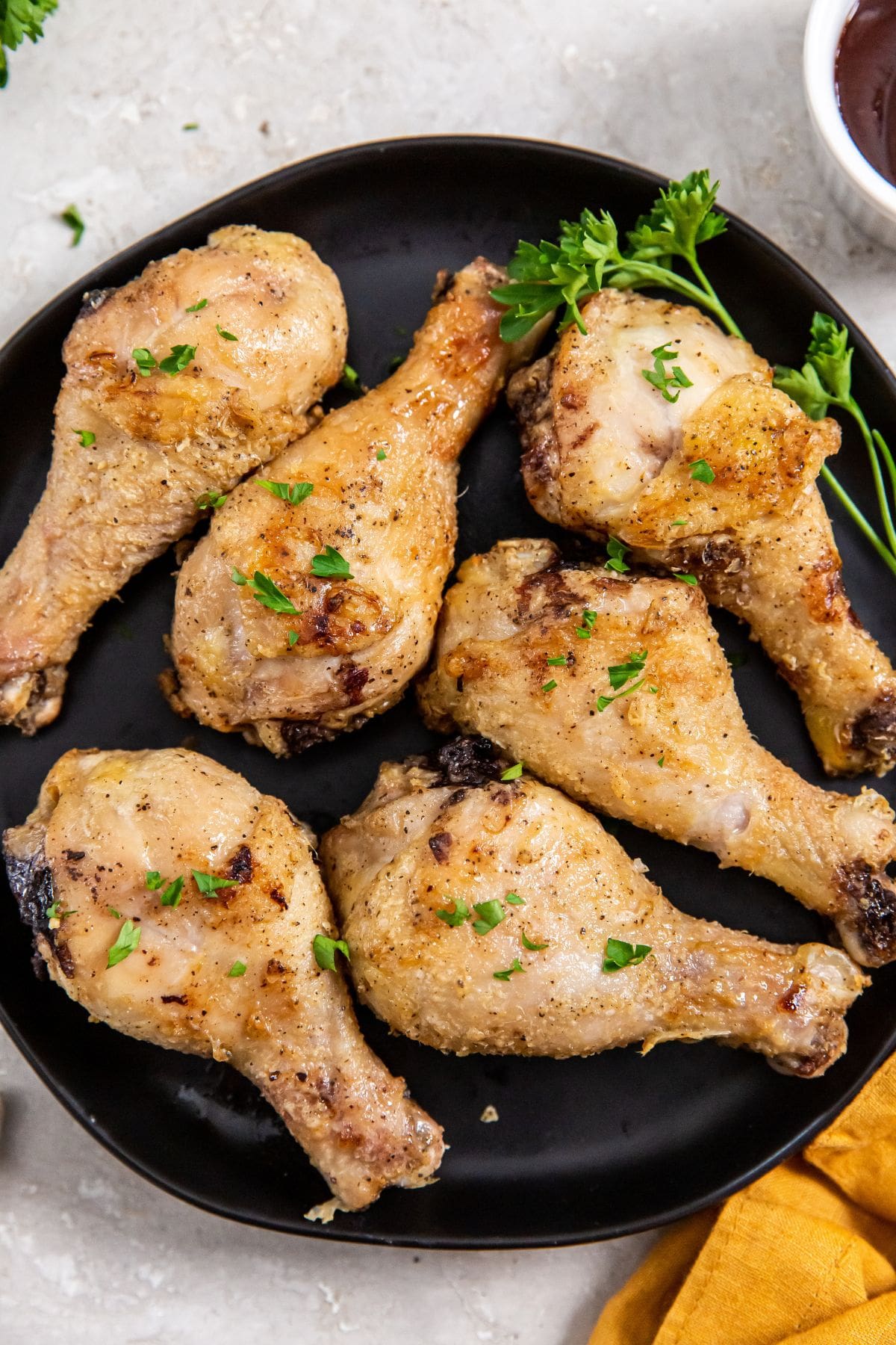 Air Fryer Crispy Chicken Legs black plate with chicken on it. orange plate in the back.