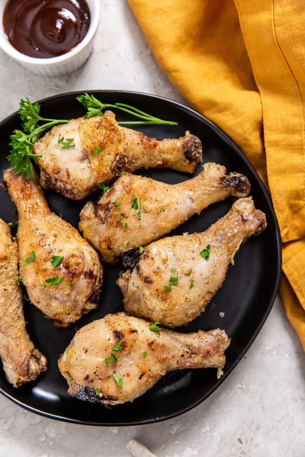 Air Fryer Crispy Chicken Legs black plate with chicken on it. orange plate in the back.
