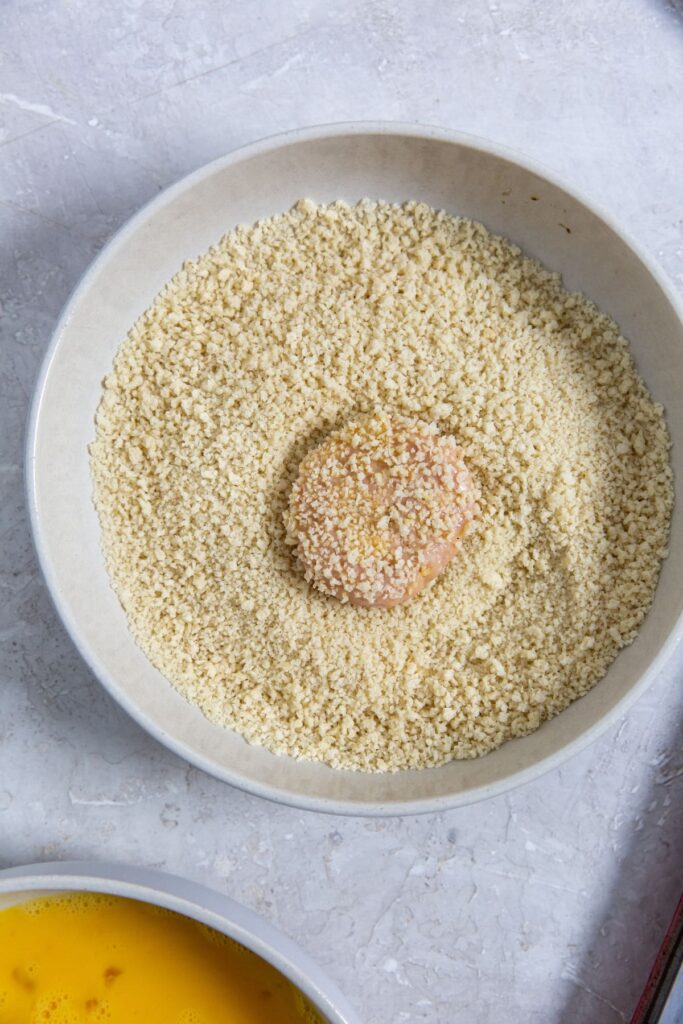 Homemade Air Fryer Chicken Nuggets Recipe bowl with bread crumbs and one chicken nuggets inside.